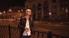 Ο ελκυστικός νεαρός άνδρας περπατά μέσω της πόλης το βράδυ και πίνει τον καφέ απόθεμα βίντεο Ο ελκυστικός νεαρός άνδρας περπατά μέσω της πόλης το βράδυ και πίνει τον καφέ απόθεμα βίντεο