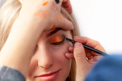 Ο καλλιτέχνης Makeup με μια βούρτσα στα χέρια με μια επίπεδη άκρη χρωματίζει το βέλος στο βλέφαρο του προτύπου, εφαρμόζει τη σύνθ στοκ φωτογραφία με δικαίωμα ελεύθερης χρήσης Ο καλλιτέχνης Makeup με μια βούρτσα στα χέρια με μια επίπεδη άκρη χρωματίζει το βέλος στο βλέφαρο του προτύπου, εφαρμόζει τη σύνθ στοκ φωτογραφία με δικαίωμα ελεύθερης χρήσης