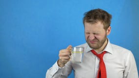 Ο νέος καυκάσιος αρσενικός επιχειρηματίας στον άσπρο δεσμό πουκάμισων και απόλυσης πίνει το νερό με το λεμόνι, υπνηλία, μπλε υπόβ απόθεμα βίντεο Ο νέος καυκάσιος αρσενικός επιχειρηματίας στον άσπρο δεσμό πουκάμισων και απόλυσης πίνει το νερό με το λεμόνι, υπνηλία, μπλε υπόβ απόθεμα βίντεο