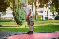 Ο νέος φορέας minigolf προσπαθεί να βάλει μια μαύρη σφαίρα στην τρύπα Στοκ Φωτογραφία Ο νέος φορέας minigolf προσπαθεί να βάλει μια μαύρη σφαίρα στην τρύπα Στοκ Φωτογραφία