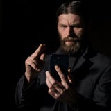 Ο παλαιός ανώτερος ιερέας οπαδών με ένα smartphone, γενειοφόρος ηληκιωμένος καλεί ένα σκοτεινό υπόβαθρο στοκ φωτογραφίες Ο παλαιός ανώτερος ιερέας οπαδών με ένα smartphone, γενειοφόρος ηληκιωμένος καλεί ένα σκοτεινό υπόβαθρο στοκ φωτογραφίες
