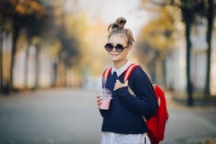 Ο όμορφος έφηβος hipster με την κόκκινη τσάντα πίνει milkshake από μια πλαστική οδό περπατήματος φλυτζανιών μεταξύ των κτηρίων Χα στοκ εικόνα με δικαίωμα ελεύθερης χρήσης Ο όμορφος έφηβος hipster με την κόκκινη τσάντα πίνει milkshake από μια πλαστική οδό περπατήματος φλυτζανιών μεταξύ των κτηρίων Χα στοκ εικόνα με δικαίωμα ελεύθερης χρήσης