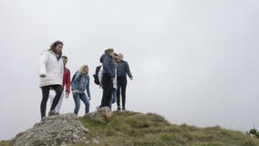 Ομάδα νέων οδοιπόρων με τα σακίδια πλάτης που στέκονται με τα χέρια που επιτυγχάνουν επάνω την κορυφή της έννοιας βουνών των νικη φιλμ μικρού μήκους Ομάδα νέων οδοιπόρων με τα σακίδια πλάτης που στέκονται με τα χέρια που επιτυγχάνουν επάνω την κορυφή της έννοιας βουνών των νικη φιλμ μικρού μήκους