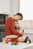 Οριζόντια φωτογραφία δύο γυναικών που αγκαλιάζουν στην κουζίνα με τις ιδιαίτερες προσοχές και το αισθησιακό χαμόγελο, που κάθεται στοκ φωτογραφία Οριζόντια φωτογραφία δύο γυναικών που αγκαλιάζουν στην κουζίνα με τις ιδιαίτερες προσοχές και το αισθησιακό χαμόγελο, που κάθεται στοκ φωτογραφία