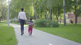 Πίσω άποψη της ελκυστικής γυναίκας αφροαμερικάνων που περπατά στο πάρκο με την λίγο γιο, που κρατά τα χέρια Χαριτωμένο παιδί φιλμ μικρού μήκους Πίσω άποψη της ελκυστικής γυναίκας αφροαμερικάνων που περπατά στο πάρκο με την λίγο γιο, που κρατά τα χέρια Χαριτωμένο παιδί φιλμ μικρού μήκους