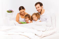 Παιχνίδι γονέων και δύο παιδιών με την ταμπλέτα στο άσπρο κρεβάτι στοκ φωτογραφία με δικαίωμα ελεύθερης χρήσης Παιχνίδι γονέων και δύο παιδιών με την ταμπλέτα στο άσπρο κρεβάτι στοκ φωτογραφία με δικαίωμα ελεύθερης χρήσης