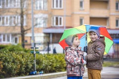Παιχνίδι μικρών παιδιών στο βροχερό θερινό πάρκο Το παιδί με τη ζωηρόχρωμη ομπρέλα ουράνιων τόξων, στεγανοποιεί το παλτό και τις Στοκ φωτογραφίες με δικαίωμα ελεύθερης χρήσης Παιχνίδι μικρών παιδιών στο βροχερό θερινό πάρκο Το παιδί με τη ζωηρόχρωμη ομπρέλα ουράνιων τόξων, στεγανοποιεί το παλτό και τις Στοκ φωτογραφίες με δικαίωμα ελεύθερης χρήσης