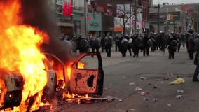 Περίπατος γραμμών αστυνομίας ταραχής προς το πλήθος μέσω της πυρκαγιάς Περίπατος γραμμών αστυνομίας ταραχής προς το πλήθος μέσω της πυρκαγιάς