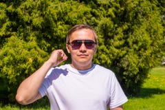 Πορτρέτο ενός ατόμου στα γυαλιά ηλίου και μιας λευκιάς μπλούζας που στέκεται έξω στο πάρκο στοκ εικόνα με δικαίωμα ελεύθερης χρήσης Πορτρέτο ενός ατόμου στα γυαλιά ηλίου και μιας λευκιάς μπλούζας που στέκεται έξω στο πάρκο στοκ εικόνα με δικαίωμα ελεύθερης χρήσης