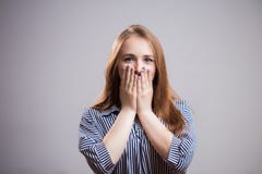 Πορτρέτο ενός νέου ελκυστικού κοριτσιού σπουδαστών που καλύπτει το στόμα της με δύο χέρια και που εξετάζει τη κάμερα σε ένα γκρίζ στοκ εικόνες με δικαίωμα ελεύθερης χρήσης Πορτρέτο ενός νέου ελκυστικού κοριτσιού σπουδαστών που καλύπτει το στόμα της με δύο χέρια και που εξετάζει τη κάμερα σε ένα γκρίζ στοκ εικόνες με δικαίωμα ελεύθερης χρήσης