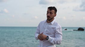Πορτρέτο ενός στοχαστικού επιτυχούς γενειοφόρου νεαρού άνδρα που στέκεται στην παραλία και που εξετάζει το ρολόι του Νέες στάσεις απόθεμα βίντεο Πορτρέτο ενός στοχαστικού επιτυχούς γενειοφόρου νεαρού άνδρα που στέκεται στην παραλία και που εξετάζει το ρολόι του Νέες στάσεις απόθεμα βίντεο