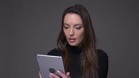 Πορτρέτο της ελκυστικής εργασίας γυναικών brunette με την ταμπλέτα που συγκεντρώνεται προσεκτική και απομονωμένος στο γκρίζο υπόβ φιλμ μικρού μήκους Πορτρέτο της ελκυστικής εργασίας γυναικών brunette με την ταμπλέτα που συγκεντρώνεται προσεκτική και απομονωμένος στο γκρίζο υπόβ φιλμ μικρού μήκους