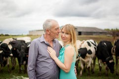 Πορτρέτο της όμορφης ανώτερης Farmer και της νέας ξανθής συζύγου του που αγκαλιάζουν μπροστά από τις γραπτές αγελάδες τους υπαίθρ στοκ φωτογραφία με δικαίωμα ελεύθερης χρήσης Πορτρέτο της όμορφης ανώτερης Farmer και της νέας ξανθής συζύγου του που αγκαλιάζουν μπροστά από τις γραπτές αγελάδες τους υπαίθρ στοκ φωτογραφία με δικαίωμα ελεύθερης χρήσης