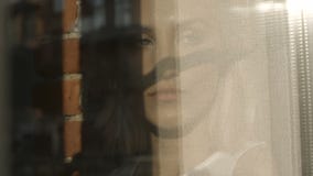 Πορτρέτο του νέου λυπημένου κοιτάγματος γυναικών μέσω του παραθύρου απόθεμα βίντεο Πορτρέτο του νέου λυπημένου κοιτάγματος γυναικών μέσω του παραθύρου απόθεμα βίντεο
