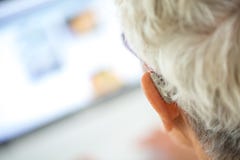 Πρεσβύτερος που φορά την ενίσχυση ακρόασης στα αυτιά της στο μέτωπο ένα lap-top στοκ εικόνες Πρεσβύτερος που φορά την ενίσχυση ακρόασης στα αυτιά της στο μέτωπο ένα lap-top στοκ εικόνες