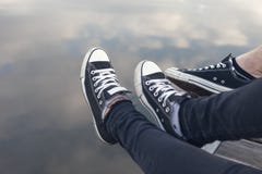 Πόδια ζευγών στα πάνινα παπούτσια που χαλαρώνουν από το νερό στοκ φωτογραφία με δικαίωμα ελεύθερης χρήσης Πόδια ζευγών στα πάνινα παπούτσια που χαλαρώνουν από το νερό στοκ φωτογραφία με δικαίωμα ελεύθερης χρήσης
