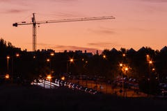 Πύργος γερανών στο ηλιοβασίλεμα σε μια πόλη με τα αναμμένα φανάρια στοκ φωτογραφία με δικαίωμα ελεύθερης χρήσης Πύργος γερανών στο ηλιοβασίλεμα σε μια πόλη με τα αναμμένα φανάρια στοκ φωτογραφία με δικαίωμα ελεύθερης χρήσης