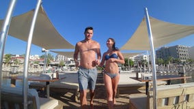 Ρομαντικό ταξίδι, εύθυμο αρσενικό με τη φίλη στα μαγιό που κρατούν τα χέρια τρέχοντας στο λιμενοβραχίονα στις καλοκαιρινές διακοπ απόθεμα βίντεο Ρομαντικό ταξίδι, εύθυμο αρσενικό με τη φίλη στα μαγιό που κρατούν τα χέρια τρέχοντας στο λιμενοβραχίονα στις καλοκαιρινές διακοπ απόθεμα βίντεο