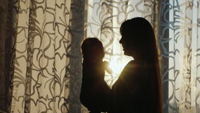 Σκιαγραφία μιας νέας μητέρας που παίζει με το μωρό από το παράθυρο στο ηλιοβασίλεμα φιλμ μικρού μήκους Σκιαγραφία μιας νέας μητέρας που παίζει με το μωρό από το παράθυρο στο ηλιοβασίλεμα φιλμ μικρού μήκους