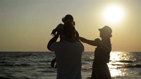 Σκοτεινές σκιαγραφίες της μητέρας στο θερινό καπέλο και του πατέρα με λίγη κόρη κοντά στη θάλασσα κατά τη διάρκεια του ηλιοβασιλέ φιλμ μικρού μήκους Σκοτεινές σκιαγραφίες της μητέρας στο θερινό καπέλο και του πατέρα με λίγη κόρη κοντά στη θάλασσα κατά τη διάρκεια του ηλιοβασιλέ φιλμ μικρού μήκους