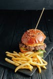 Σπιτικό juicy burger με τις τηγανιτές πατάτες στο σκοτεινό ξύλινο πίνακα στοκ φωτογραφία Σπιτικό juicy burger με τις τηγανιτές πατάτες στο σκοτεινό ξύλινο πίνακα στοκ φωτογραφία
