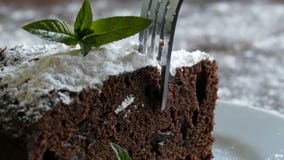 Σπιτικό ψημένο brownie σοκολάτας κέικ που καλύπτεται με την κονιοποιημένη ζάχαρη σε ένα άσπρο πιάτο που διακοσμείται με τα φύλλα απόθεμα βίντεο Σπιτικό ψημένο brownie σοκολάτας κέικ που καλύπτεται με την κονιοποιημένη ζάχαρη σε ένα άσπρο πιάτο που διακοσμείται με τα φύλλα απόθεμα βίντεο