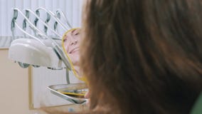 Στενή άποψη ενός νέου χαμογελώντας κοριτσιού στον καθρέφτη Ο ασθενής κάθεται σε μια οδοντική καρέκλα μετά από τη διαδικασία για φιλμ μικρού μήκους Στενή άποψη ενός νέου χαμογελώντας κοριτσιού στον καθρέφτη Ο ασθενής κάθεται σε μια οδοντική καρέκλα μετά από τη διαδικασία για φιλμ μικρού μήκους