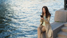 Συνεδρίαση smartphone χρήσης επιχειρησιακών γυναικών στο ανάχωμα ποταμών απόθεμα βίντεο Συνεδρίαση smartphone χρήσης επιχειρησιακών γυναικών στο ανάχωμα ποταμών απόθεμα βίντεο