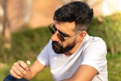 Συνεδρίαση τύπων Hipster που κρατά υπαίθρια ένα λουλούδι στοκ φωτογραφία Συνεδρίαση τύπων Hipster που κρατά υπαίθρια ένα λουλούδι στοκ φωτογραφία