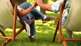 Συνταξιούχος συνεδρίαση ζευγών στις καρέκλες γεφυρών που κρατά τα χέρια απόθεμα βίντεο Συνταξιούχος συνεδρίαση ζευγών στις καρέκλες γεφυρών που κρατά τα χέρια απόθεμα βίντεο