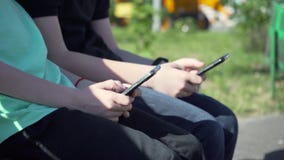 Τα αγόρια με το μαύρο smartphone κάθονται στον πάγκο Τα μικρά παιδιά με το τηλέφωνο κυττάρων κάθονται στον πάγκο στον κήπο Τα παι φιλμ μικρού μήκους Τα αγόρια με το μαύρο smartphone κάθονται στον πάγκο Τα μικρά παιδιά με το τηλέφωνο κυττάρων κάθονται στον πάγκο στον κήπο Τα παι φιλμ μικρού μήκους