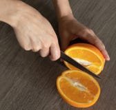 Τα ανθρώπινα χέρια με ένα μαχαίρι κόβουν το πορτοκάλι στο μισό στοκ φωτογραφία με δικαίωμα ελεύθερης χρήσης Τα ανθρώπινα χέρια με ένα μαχαίρι κόβουν το πορτοκάλι στο μισό στοκ φωτογραφία με δικαίωμα ελεύθερης χρήσης