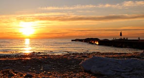 Τα λαμπρά πορτοκαλιά και κίτρινα χρώματα στο ηλιοβασίλεμα πέρα από τη λίμνη Huron ως χειμερινούς χιόνι και πάγο λειώνουν στοκ φωτογραφίες με δικαίωμα ελεύθερης χρήσης Τα λαμπρά πορτοκαλιά και κίτρινα χρώματα στο ηλιοβασίλεμα πέρα από τη λίμνη Huron ως χειμερινούς χιόνι και πάγο λειώνουν στοκ φωτογραφίες με δικαίωμα ελεύθερης χρήσης
