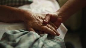 Τηγάνι των ηλικιωμένων χεριών εκμετάλλευσης προσώπων στο κρεβάτι όπου ξαπλώνει Τηγάνι των ηλικιωμένων χεριών εκμετάλλευσης προσώπων στο κρεβάτι όπου ξαπλώνει