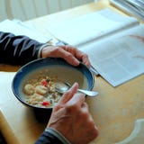 Το άτομο με παραδίδει το πρωί, τρώγοντας oatmeal προγευμάτων με τις φράουλες και τις μπανάνες στον πίνακα κουζινών του στοκ εικόνα Το άτομο με παραδίδει το πρωί, τρώγοντας oatmeal προγευμάτων με τις φράουλες και τις μπανάνες στον πίνακα κουζινών του στοκ εικόνα