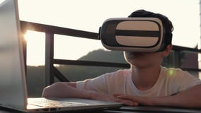 Το αγόρι παίζει στον υπολογιστή στα γυαλιά εικονικής πραγματικότητας στο ηλιοβασίλεμα στο ηλιοβασίλεμα Η έννοια σύγχρονου Το αγόρι παίζει στον υπολογιστή στα γυαλιά εικονικής πραγματικότητας στο ηλιοβασίλεμα στο ηλιοβασίλεμα Η έννοια σύγχρονου
