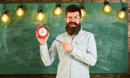 Το γενειοφόρο hipster κρατά το ρολόι, πίνακας κιμωλίας στο υπόβαθρο Ο δάσκαλος eyeglasses κρατά το ξυπνητήρι και τη μάνδρα πειθαρ στοκ εικόνες Το γενειοφόρο hipster κρατά το ρολόι, πίνακας κιμωλίας στο υπόβαθρο Ο δάσκαλος eyeglasses κρατά το ξυπνητήρι και τη μάνδρα πειθαρ στοκ εικόνες