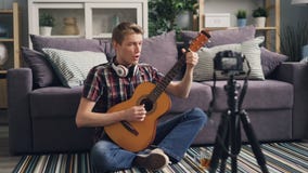 Το επιτυχές vlogger νεαρών άνδρων καταγράφει το βίντεο που παίζει την κιθάρα και που τραγουδά τη συνεδρίαση στο πάτωμα στο σπίτι φιλμ μικρού μήκους Το επιτυχές vlogger νεαρών άνδρων καταγράφει το βίντεο που παίζει την κιθάρα και που τραγουδά τη συνεδρίαση στο πάτωμα στο σπίτι φιλμ μικρού μήκους