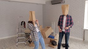 Το ευτυχές ζεύγος έχει τη διασκέδαση στο νέο διαμέρισμά τους με τις τσάντες χαρτονιού στα κεφάλια τους φιλμ μικρού μήκους Το ευτυχές ζεύγος έχει τη διασκέδαση στο νέο διαμέρισμά τους με τις τσάντες χαρτονιού στα κεφάλια τους φιλμ μικρού μήκους