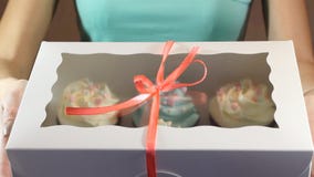 Το διακοσμητικό κιβώτιο δώρων έδεσε με τα cupcakes μια τυρκουάζ κορδέλλα στα θηλυκά χέρια φιλμ μικρού μήκους Το διακοσμητικό κιβώτιο δώρων έδεσε με τα cupcakes μια τυρκουάζ κορδέλλα στα θηλυκά χέρια φιλμ μικρού μήκους