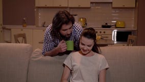 Το κορίτσι κάθεται στον καναπέ και εργάζεται με την ταμπλέτα Ο τύπος έρχεται από την κουζίνα και stoppes πίσω από τη γυναίκα Κρατ απόθεμα βίντεο Το κορίτσι κάθεται στον καναπέ και εργάζεται με την ταμπλέτα Ο τύπος έρχεται από την κουζίνα και stoppes πίσω από τη γυναίκα Κρατ απόθεμα βίντεο