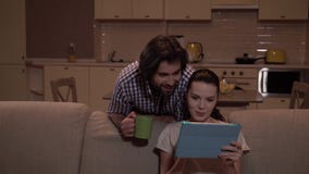 Το κορίτσι κάθεται στον καναπέ και χρησιμοποιεί την ταμπλέτα Εξετάζει το και παρουσιάζει στον τύπο Στέκεται πίσω από τον καναπέ κ απόθεμα βίντεο Το κορίτσι κάθεται στον καναπέ και χρησιμοποιεί την ταμπλέτα Εξετάζει το και παρουσιάζει στον τύπο Στέκεται πίσω από τον καναπέ κ απόθεμα βίντεο