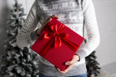 Το κορίτσι στο πουλόβερ ενός νέου έτους με τα ελάφια κρατά υπό εξέταση ένα κόκκινο κιβώτιο με ένα δώρο και ένα κώλυμα στα πλαίσια στοκ φωτογραφία με δικαίωμα ελεύθερης χρήσης Το κορίτσι στο πουλόβερ ενός νέου έτους με τα ελάφια κρατά υπό εξέταση ένα κόκκινο κιβώτιο με ένα δώρο και ένα κώλυμα στα πλαίσια στοκ φωτογραφία με δικαίωμα ελεύθερης χρήσης