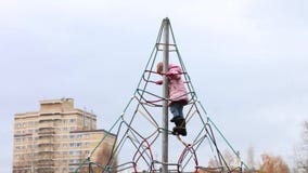 Το μικρό κορίτσι στα θερμά ενδύματα αναρριχείται και κρεμά στην παιδική χαρά φιλμ μικρού μήκους Το μικρό κορίτσι στα θερμά ενδύματα αναρριχείται και κρεμά στην παιδική χαρά φιλμ μικρού μήκους
