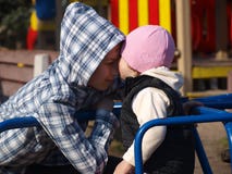 Το μικρό κορίτσι τεντώνει για να φιλήσει τον αδελφό εφήβων της καθμένος στο ιπποδρόμιο στοκ εικόνα Το μικρό κορίτσι τεντώνει για να φιλήσει τον αδελφό εφήβων της καθμένος στο ιπποδρόμιο στοκ εικόνα