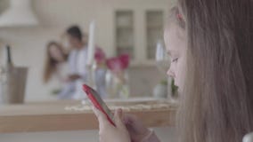 Το μικρό παιχνίδι κοριτσιών με το κινητό τηλέφωνο και στο υπόβαθρο είναι η μητέρα και ο πατέρας της στη μεγάλη κουζίνα φιλμ μικρού μήκους Το μικρό παιχνίδι κοριτσιών με το κινητό τηλέφωνο και στο υπόβαθρο είναι η μητέρα και ο πατέρας της στη μεγάλη κουζίνα φιλμ μικρού μήκους