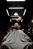 Το μοντέρνο barbershop Ο κουρέας μόδας τακτοποιεί τη γενειάδα της βάναυσης συνεδρίασης ατόμων στην πολυθρόνα στοκ φωτογραφίες Το μοντέρνο barbershop Ο κουρέας μόδας τακτοποιεί τη γενειάδα της βάναυσης συνεδρίασης ατόμων στην πολυθρόνα στοκ φωτογραφίες