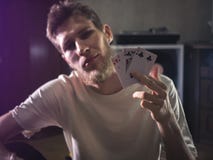 Το νέο γενειοφόρο άτομο στις περιστασιακές κάρτες εκμετάλλευσης playng παρουσιάζει κάποιο πορτρέτο τεχνασμάτων στο σπίτι στοκ φωτογραφίες Το νέο γενειοφόρο άτομο στις περιστασιακές κάρτες εκμετάλλευσης playng παρουσιάζει κάποιο πορτρέτο τεχνασμάτων στο σπίτι στοκ φωτογραφίες
