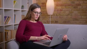 Το νέο και όμορφο θηλυκό brunette freelancer στα γυαλιά που λειτουργούν με το lap-top γυρίζει στη κάμερα και χαμογελά στο σπίτι απόθεμα βίντεο Το νέο και όμορφο θηλυκό brunette freelancer στα γυαλιά που λειτουργούν με το lap-top γυρίζει στη κάμερα και χαμογελά στο σπίτι απόθεμα βίντεο