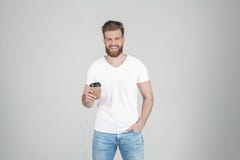 Το πορτρέτο ενός όμορφου προκλητικού γενειοφόρου ατόμου που ντύνεται σε μια άσπρη μπλούζα κρατά ένα φλιτζάνι του καφέ στο χέρι το στοκ εικόνες με δικαίωμα ελεύθερης χρήσης Το πορτρέτο ενός όμορφου προκλητικού γενειοφόρου ατόμου που ντύνεται σε μια άσπρη μπλούζα κρατά ένα φλιτζάνι του καφέ στο χέρι το στοκ εικόνες με δικαίωμα ελεύθερης χρήσης